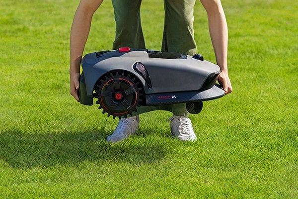 Muž zvedá robotickou sekačku ze země.